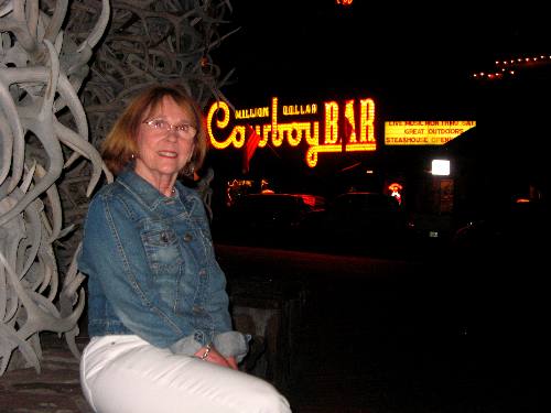 Joyce Hendris in front of an elk horn arch in Jackson, Wyoming Town Square with lights from Million Dollar Cowboy Bar in the background