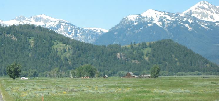 Buildings on Mormon Row visible across Antelope Flats with the snow covered slopes of the Teton Range visible in the distance